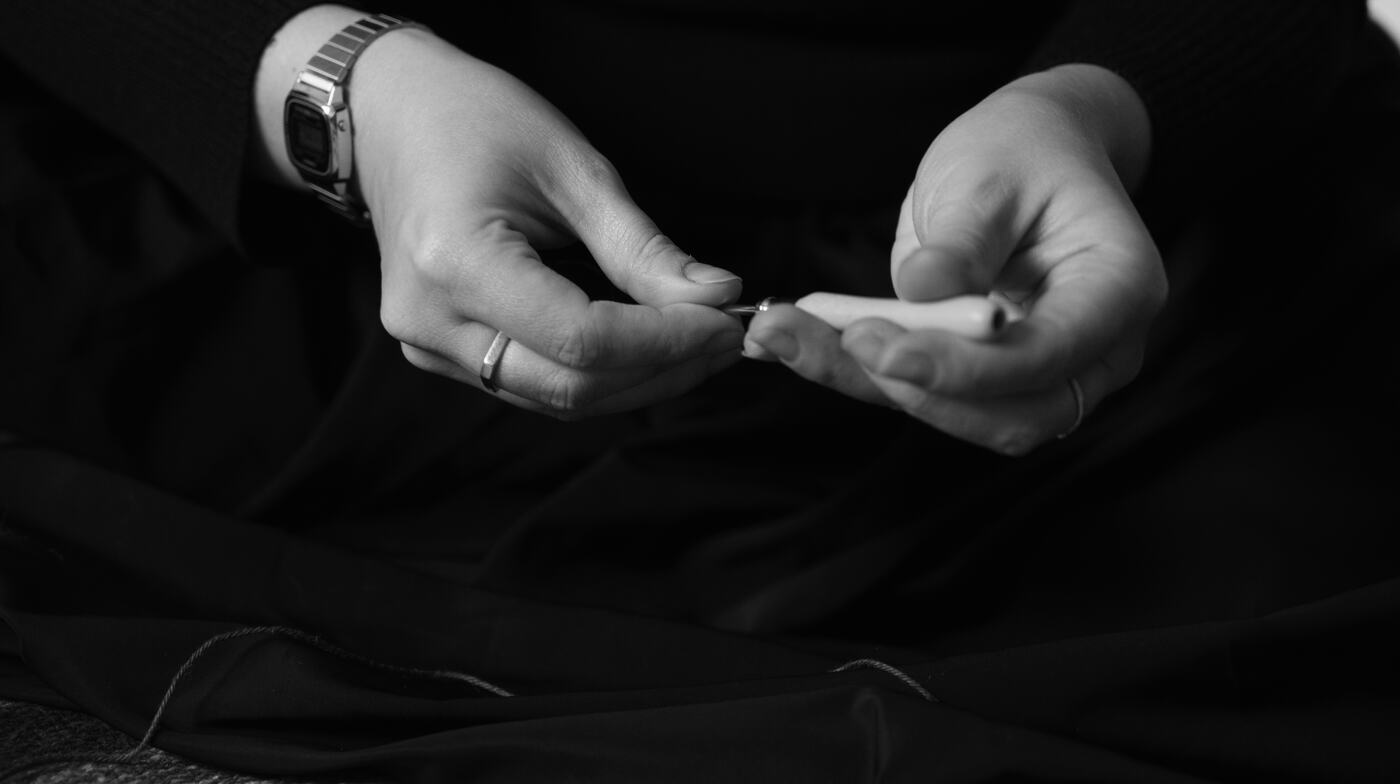 As mãos de Vitória enfiando a lã em uma agulha de punch needle, em preto e branco