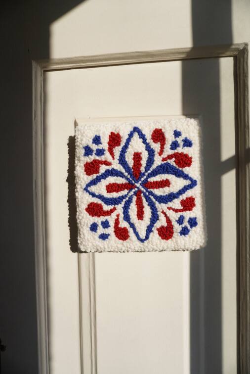 Azulejo em lã branca, azul e vermelha, pendurado numa porta branca