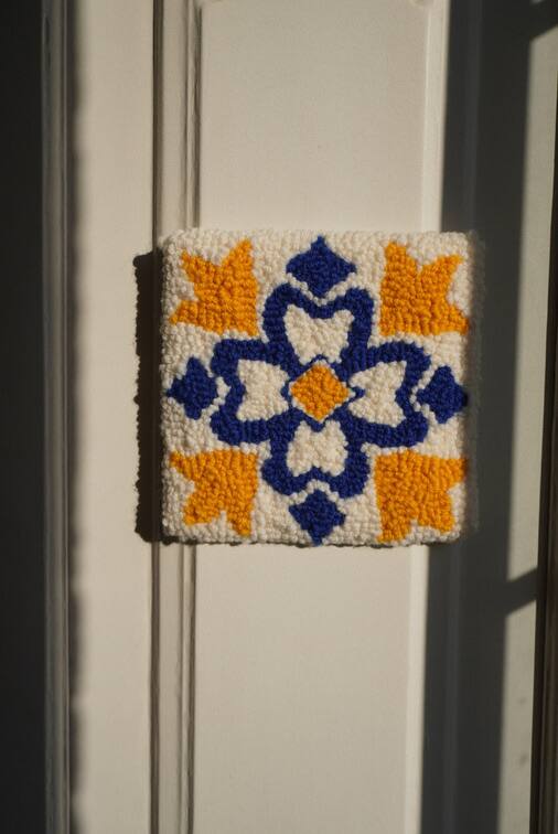 Azulejo em lã branca, azul e laranja, pendurado numa porta branca