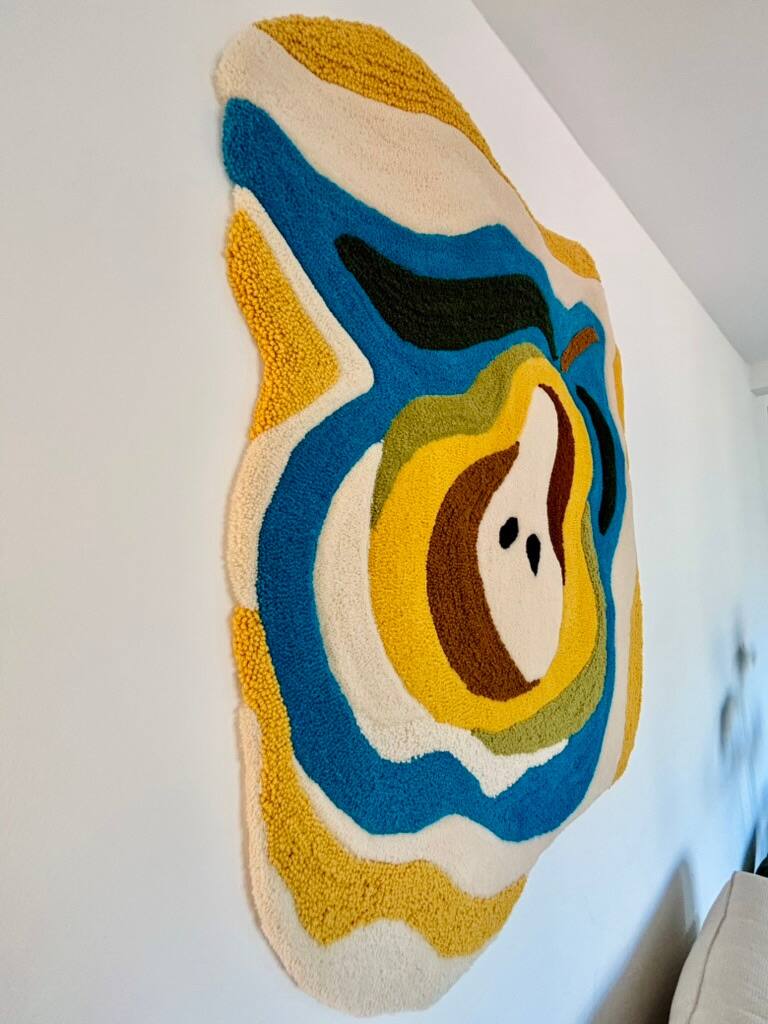 Peça de parede de contorno ondulado com uma pera cortada ao meio, em azul, amarelo, verde e marrom