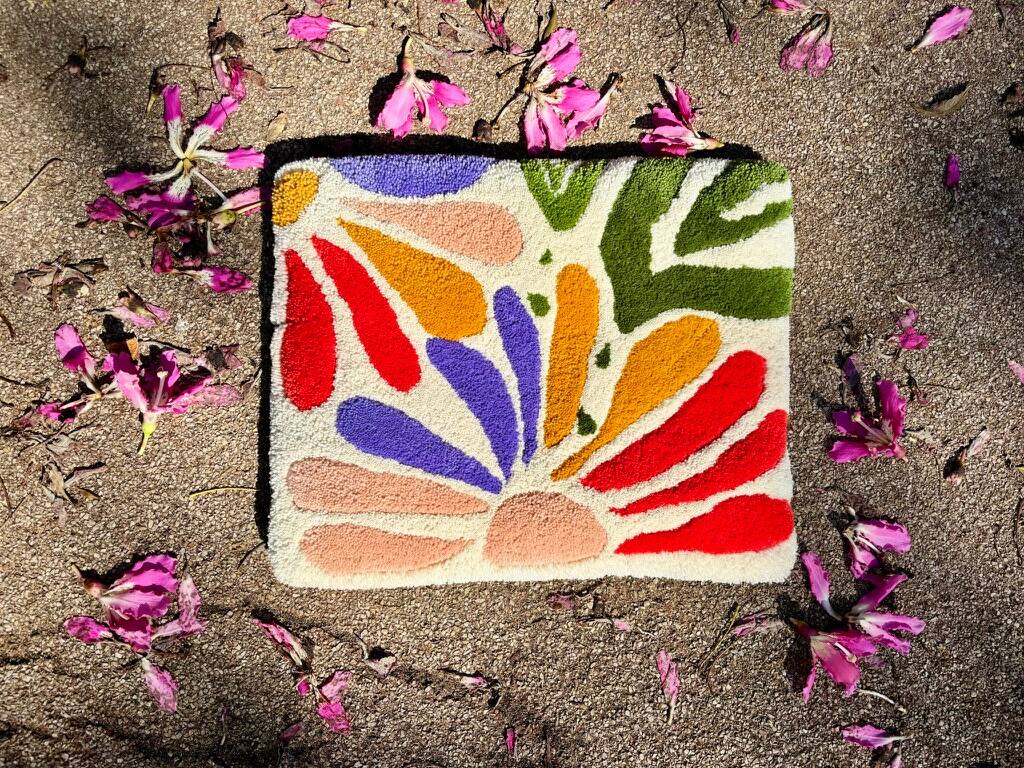 Tapete pequeno com pétalas coloridas, sobre a areia entre flores caídas