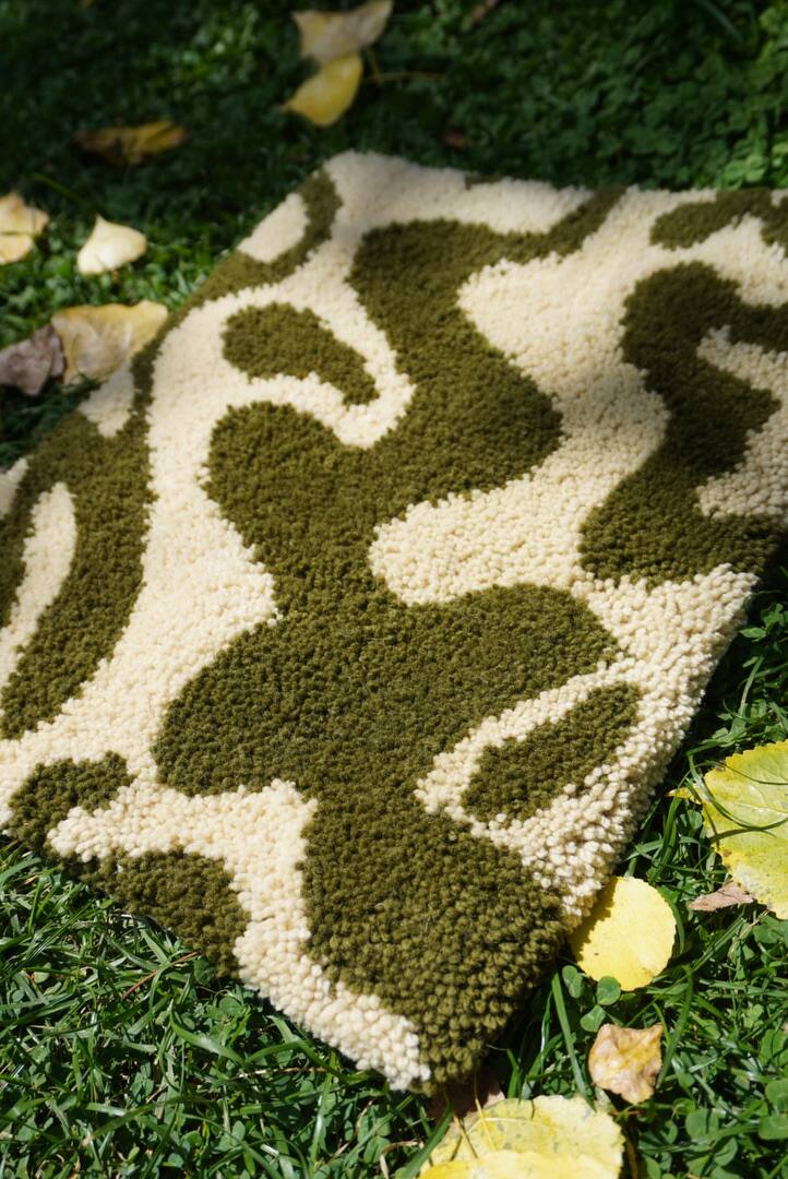 Tapete em verde-oliva e creme com formas orgânicas, sobre a grama entre folhas amarelas